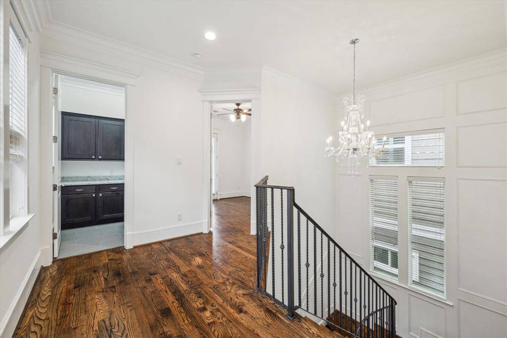 This beautifully designed second-floor landing serves as both a functional and stylish transition space. A stunning crystal chandelier adds a touch of sophistication, complementing the intricate wall paneling and oversized windows that fill the space with natural light. The rich hardwood floors continue throughout, seamlessly connecting the upper-level living areas.