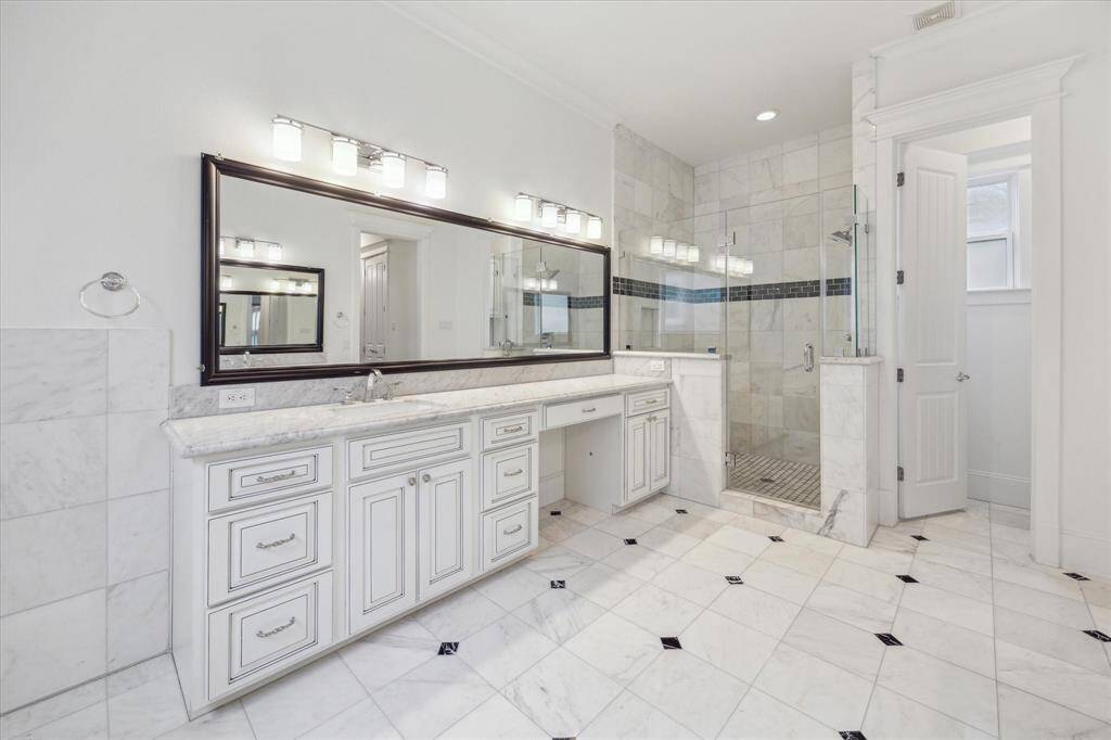 The oversized walk-in shower is a true retreat, featuring floor-to-ceiling tile, a sleek glass enclosure, and a contrasting accent band for a sophisticated touch. Thoughtful lighting and polished fixtures add to the bright and inviting ambiance, creating a spa-like experience in the comfort of home.