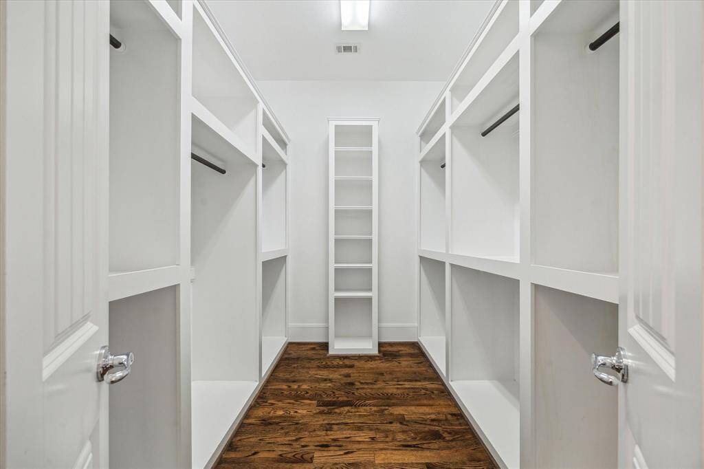 Maximized storage and elegant design come together in this spacious walk-in closet. Custom-built shelving, hanging racks, and open compartments provide ample space for clothing, accessories, and shoes. A centrally positioned shelving tower offers additional organization, while the rich hardwood flooring adds warmth and sophistication.