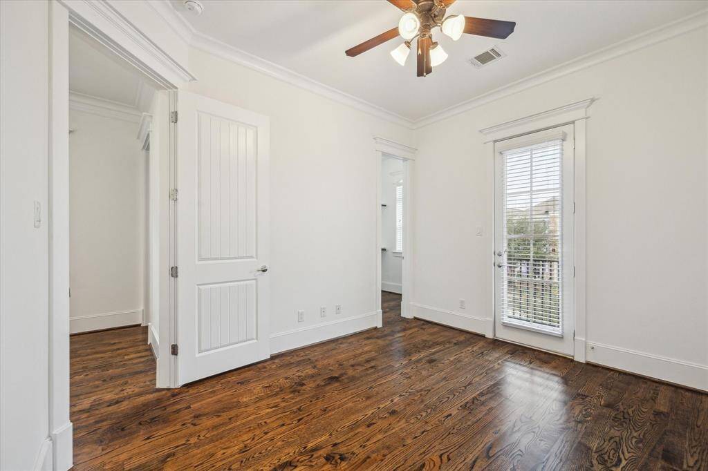 This well-appointed secondary bedroom offers a tranquil retreat with classic design elements and abundant natural light. Warm hardwood floors extend throughout, complementing the crisp white walls and crown molding. A set of French doors opens to a private balcony, providing fresh air and a charming view of the neighborhood.