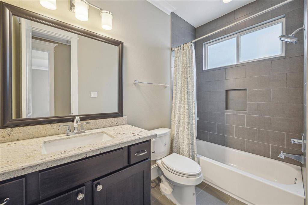 Designed with both style and functionality in mind, this garage apartment bathroom features contemporary finishes and thoughtful details. A dark wood vanity with a granite countertop provides ample storage, while a framed mirror and modern lighting enhance the space.