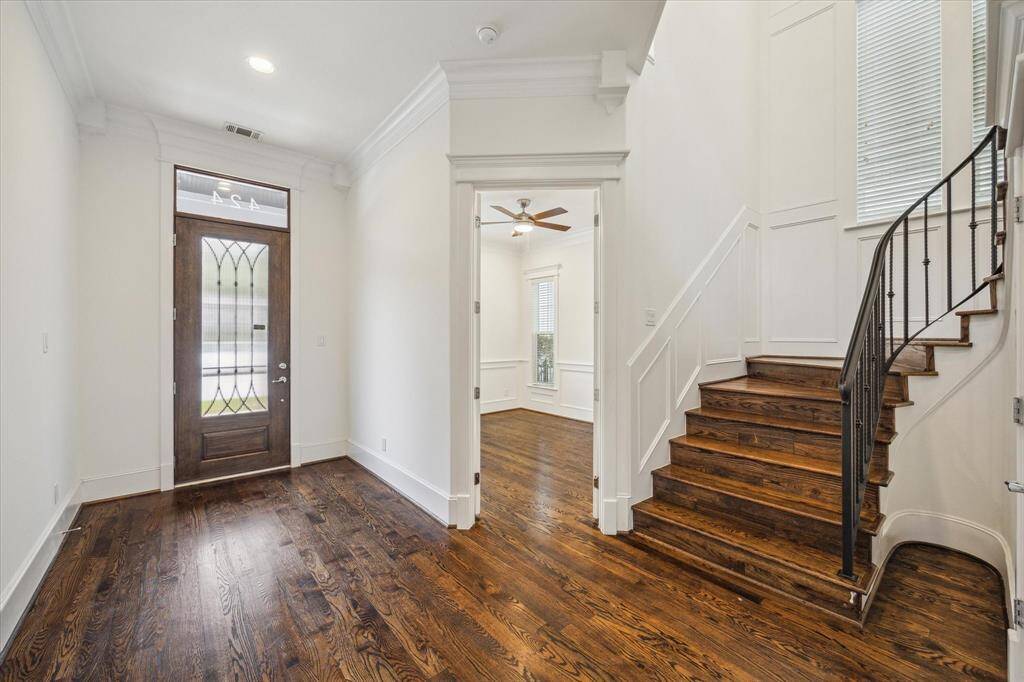 The entryway boasts stunning hardwood floors that extend throughout, complemented by crisp white walls and exquisite crown molding. A statement-making staircase with wrought iron accents adds an architectural focal point, while natural light pours in from well-placed windows. The glass-paneled front door enhances the home’s curb appeal and allows for a bright, airy ambiance.