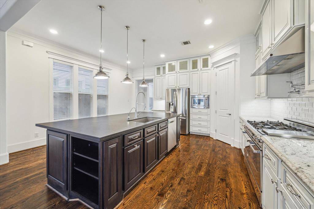 Designed for both style and function, this gourmet kitchen is the heart of the home. Custom cabinetry with glass-front accents, a sleek subway tile backsplash, and a professional-grade stainless steel gas range create a refined yet practical cooking space. The oversized island, finished in a striking dark wood tone, offers ample prep space, additional storage, and a breakfast bar illuminated by polished pendant lighting.