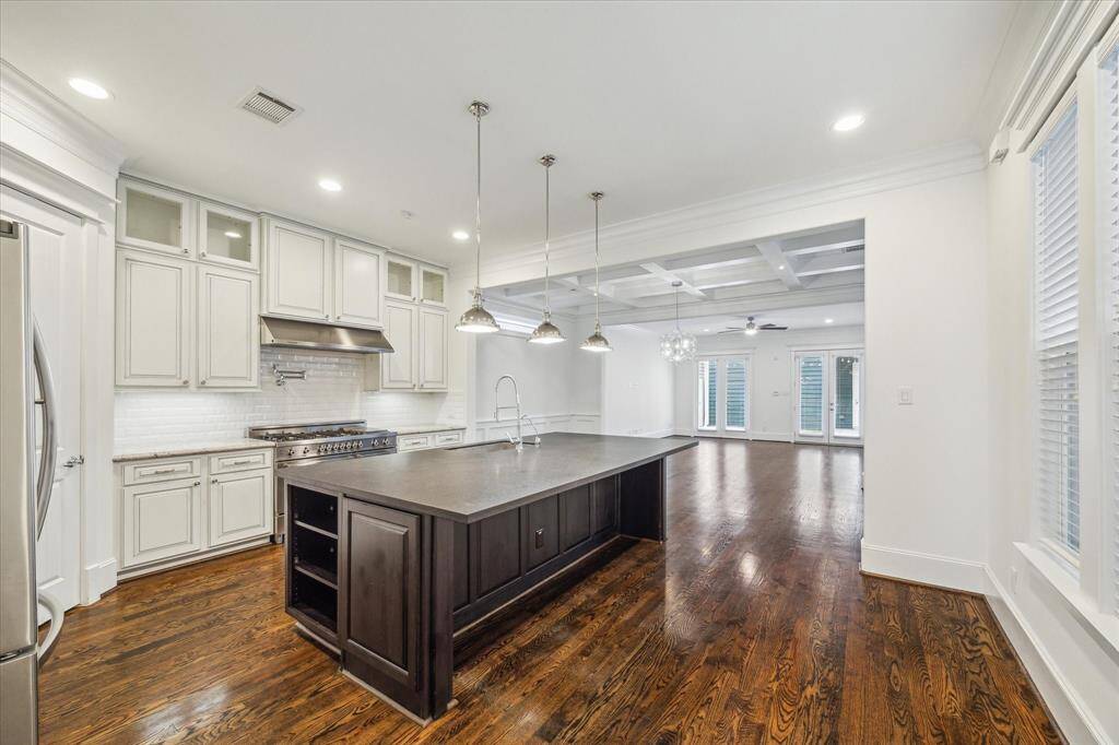 Beyond the kitchen, the open living area exudes sophistication with a coffered ceiling, rich hardwood floors, and expansive windows that bathe the space in natural light. French doors lead to the backyard, enhancing indoor-outdoor living. Whether entertaining guests or enjoying a quiet evening, this thoughtfully designed layout provides the perfect balance of elegance and comfort.