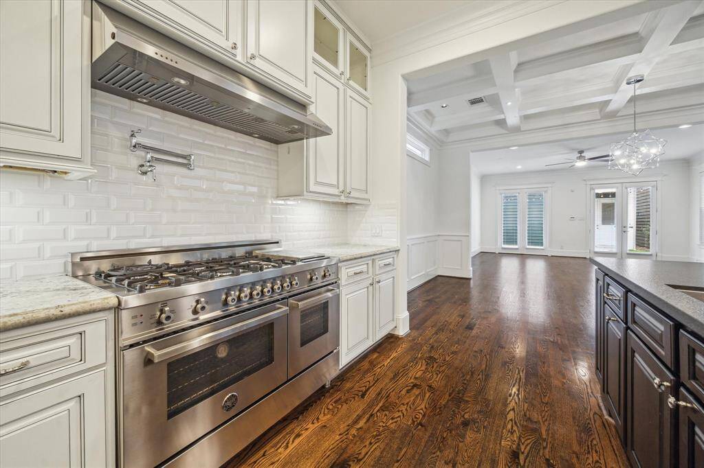 Every detail of this gourmet kitchen is designed to impress. Anchored by a top-of-the-line stainless steel gas range with double ovens, this space is ready for everything from casual meals to elaborate dinner parties. A sleek pot filler adds convenience, while the custom cabinetry, complete with glass-front accents, offers ample storage. The crisp white subway tile backsplash enhances the space’s bright and airy feel, complementing the rich hardwood floors.