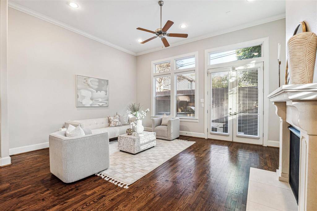 Bright and spacious living room with hardwood floors, high ceilings, and large windows. Features a cozy seating area, modern fireplace, and ample natural light from glass doors leading to an outdoor space.