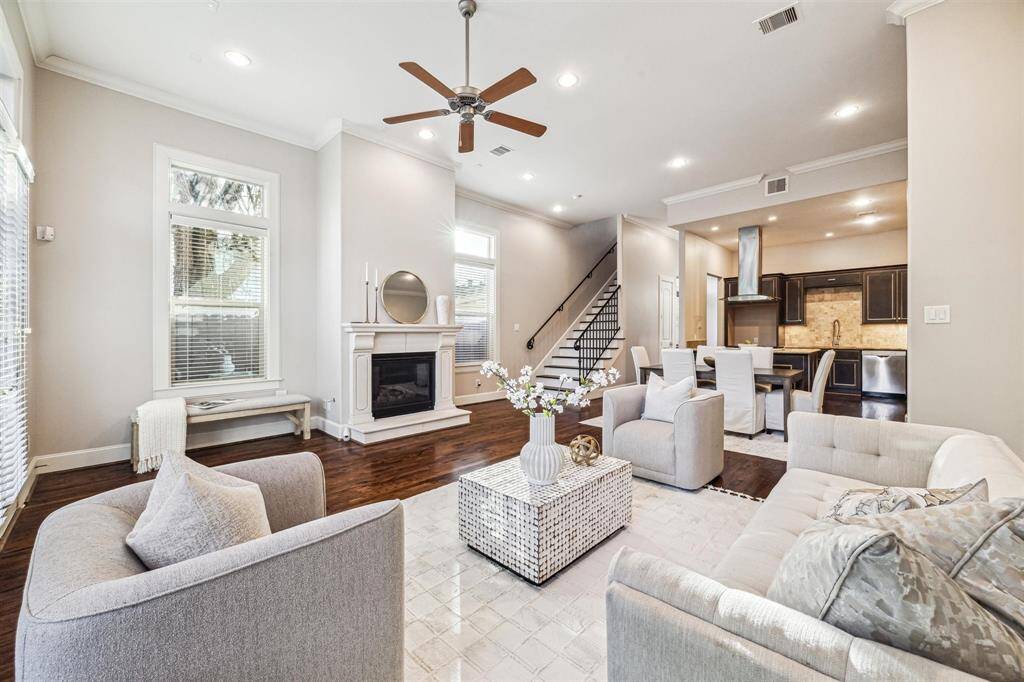 Spacious, modern open-concept living area with high ceilings, a cozy fireplace, and elegant hardwood floors. The room is well-lit with large windows, and the adjacent kitchen features sleek cabinetry and stainless steel appliances. A staircase leads to the upper level, adding to the home's charm.