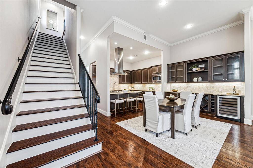This modern home features an open-concept kitchen and dining area with sleek cabinetry, stainless steel appliances, and a large island. The space is highlighted by hardwood floors and ample lighting. A staircase with elegant railings leads to the upper level, adding to the home's stylish appeal.