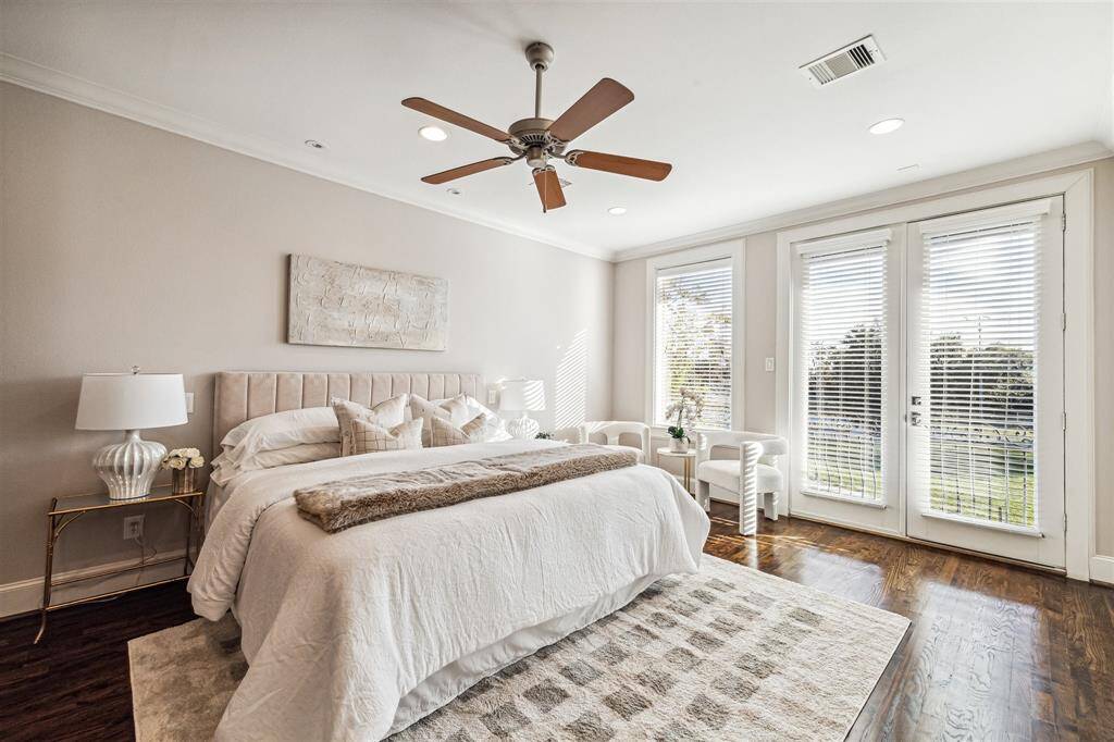 Primary bedroom features hardwood floors, a ceiling fan, and large windows with French doors leading to a balcony.