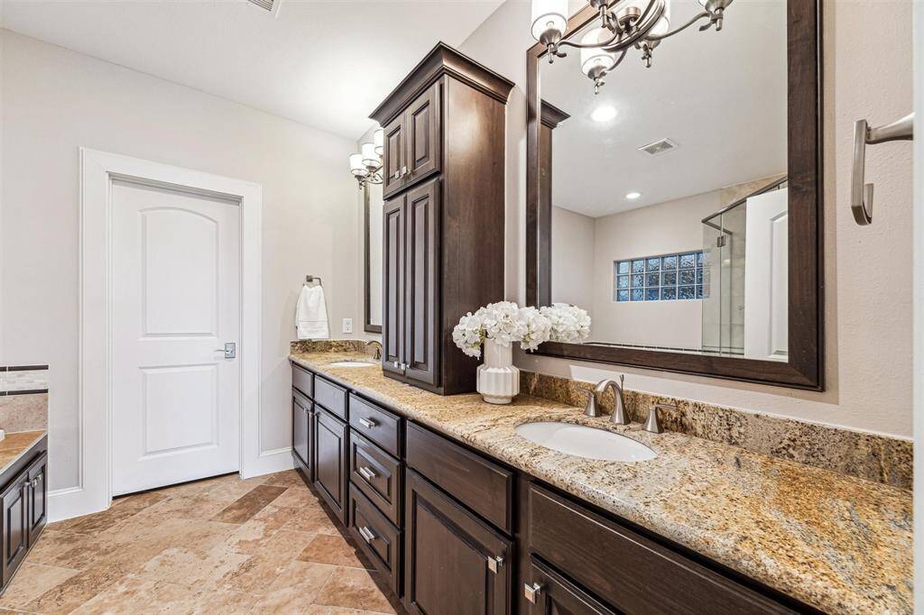 This elegant bathroom features dual sinks with dark wood cabinetry, granite countertops, and a large mirror. The space is accented by a stylish light fixture and a neutral color palette, with a separate shower area visible in the background.