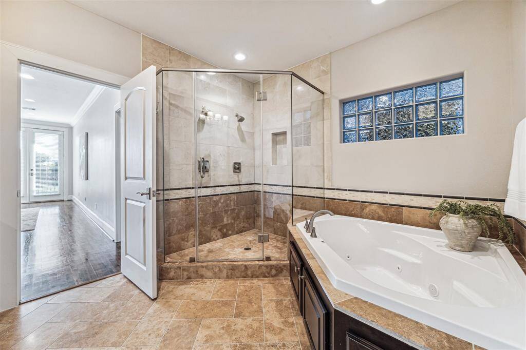 This modern bathroom features a spacious glass-enclosed shower, a luxurious corner bathtub, and elegant tile flooring.