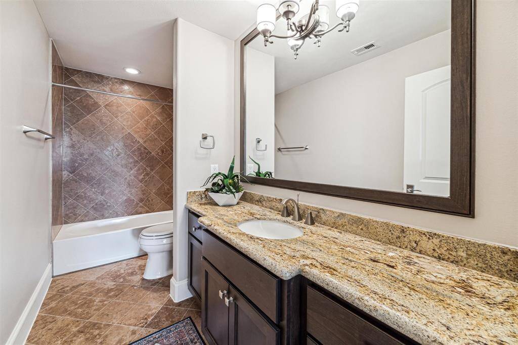 Third floor bathroom features a granite countertop with a single sink, dark wood cabinetry, and a large mirror. It includes a shower-tub combo with travertine tile accents and a modern lighting.
