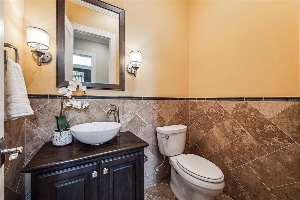 A modern half-bathroom featuring elegant tile wainscoting, a sleek dark wood vanity with a vessel sink, and contemporary lighting fixtures.
