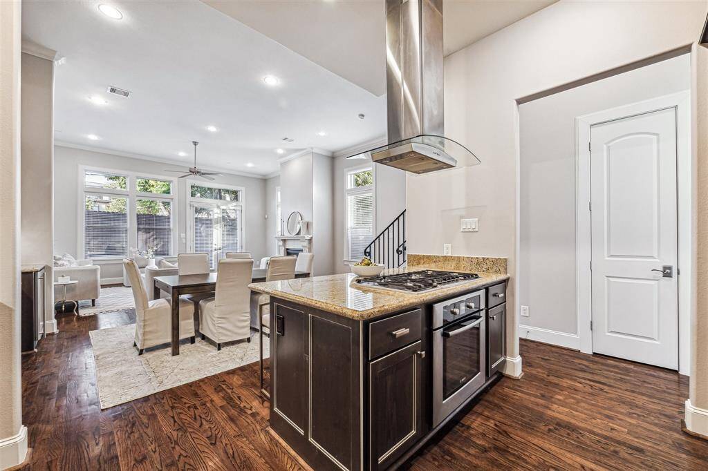 Open-concept living space features a modern kitchen with a central island and gas stove, seamlessly flowing into a bright dining and living area with large windows, hardwood floors, and a cozy fireplace.