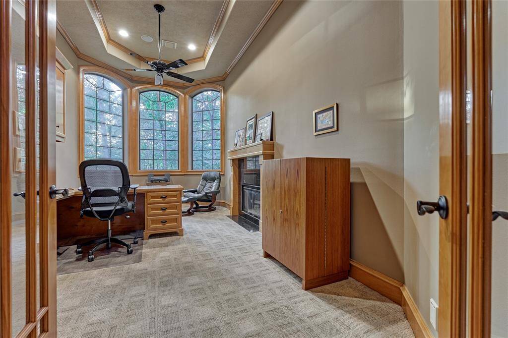 Warm wood tones accentuate the executive study featuring a tiered ceiling, cozy fireplace and designer carpeting.