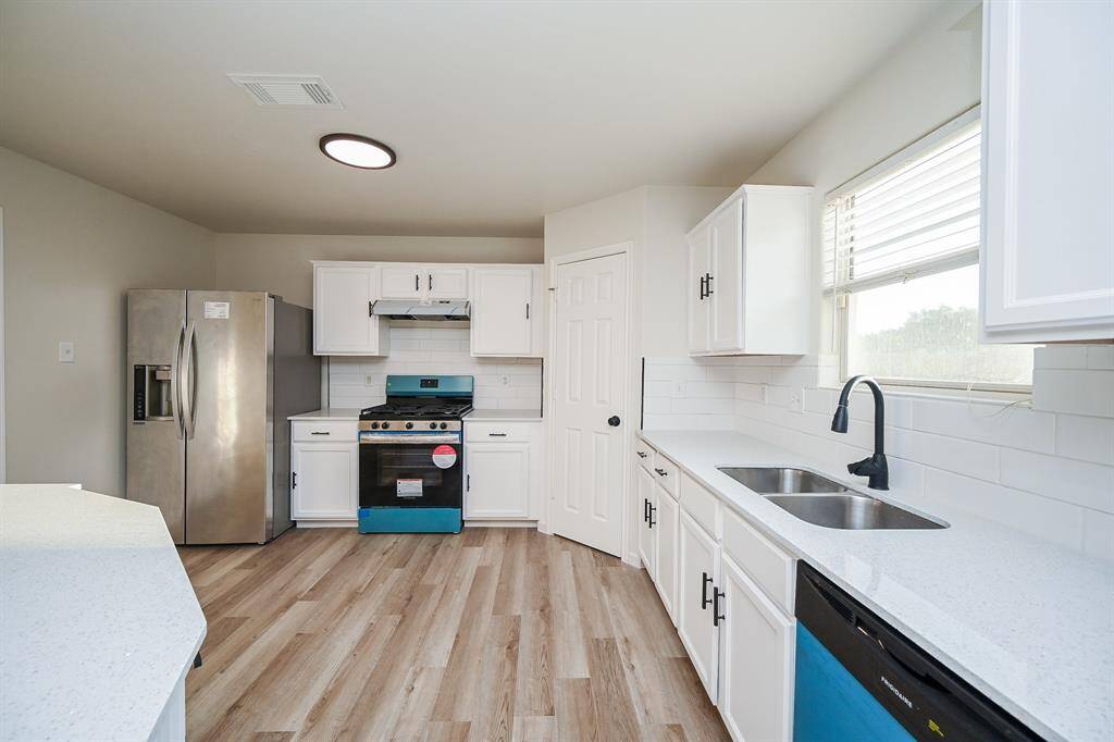 Modern kitchen with white cabinetry, stainless steel appliances, and wood-look flooring. Features a double sink, ample counter space, and natural light from a large window.