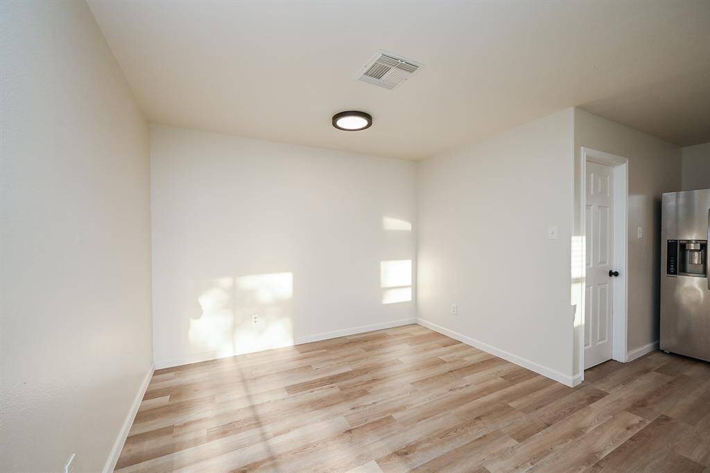 Bright and cozy dining room with light wood flooring, white walls, and a modern ceiling light. It features a stainless steel refrigerator