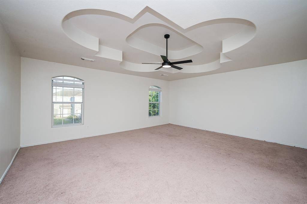 Spacious primary room with neutral walls and carpet, featuring a unique, modern ceiling design with a central fan. Two large windows provide ample natural light.