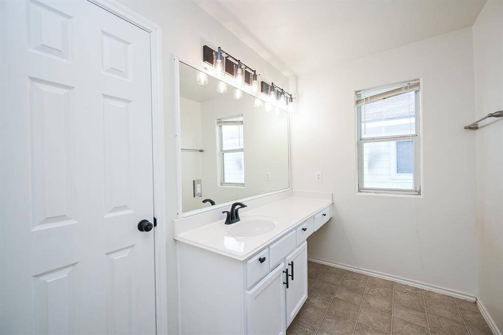 Spacious and bright primary bathroom featuring a sleek vanity, ample counter space, and modern fixtures. Natural light pours in through the window, creating a refreshing atmosphere.