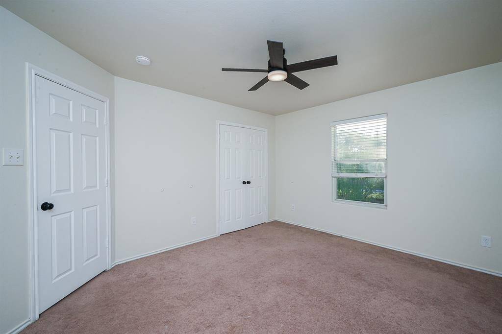 This room features neutral walls and carpet, a ceiling fan, a window for natural light, and a closet with double doors, offering a cozy and functional space.