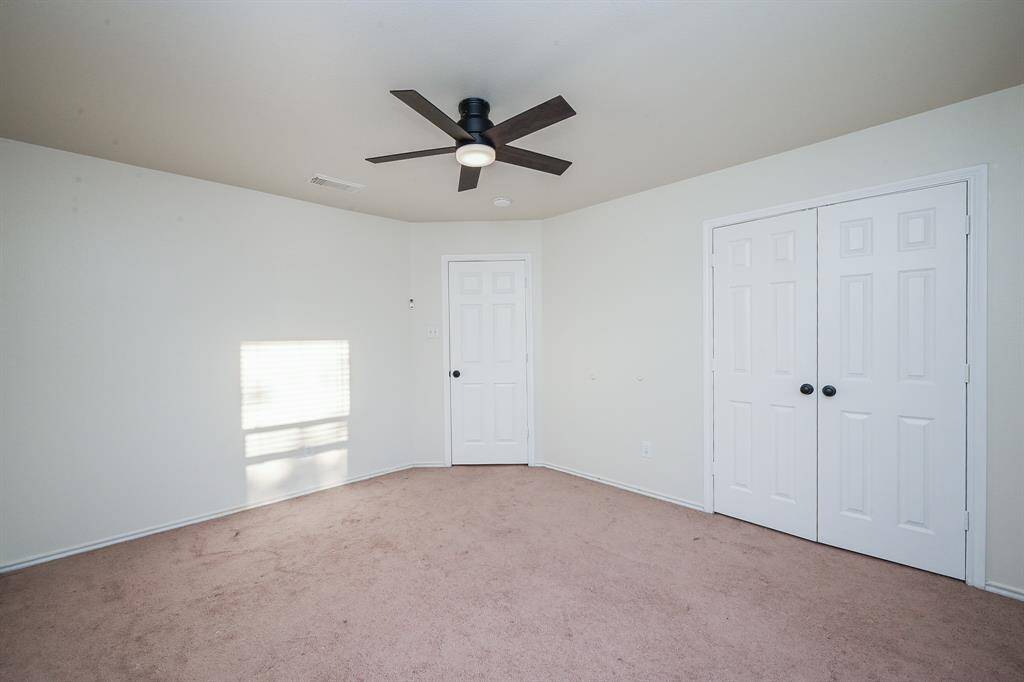 This photo shows a bright room with neutral walls and carpeting. It features a ceiling fan and double-door closet, making it a versatile space for various uses.