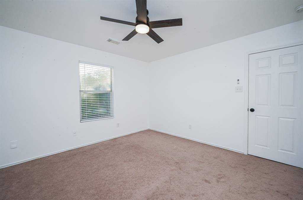 Spacious bedroom featuring a modern ceiling fan, plush carpeting, and ample natural light through a large window.