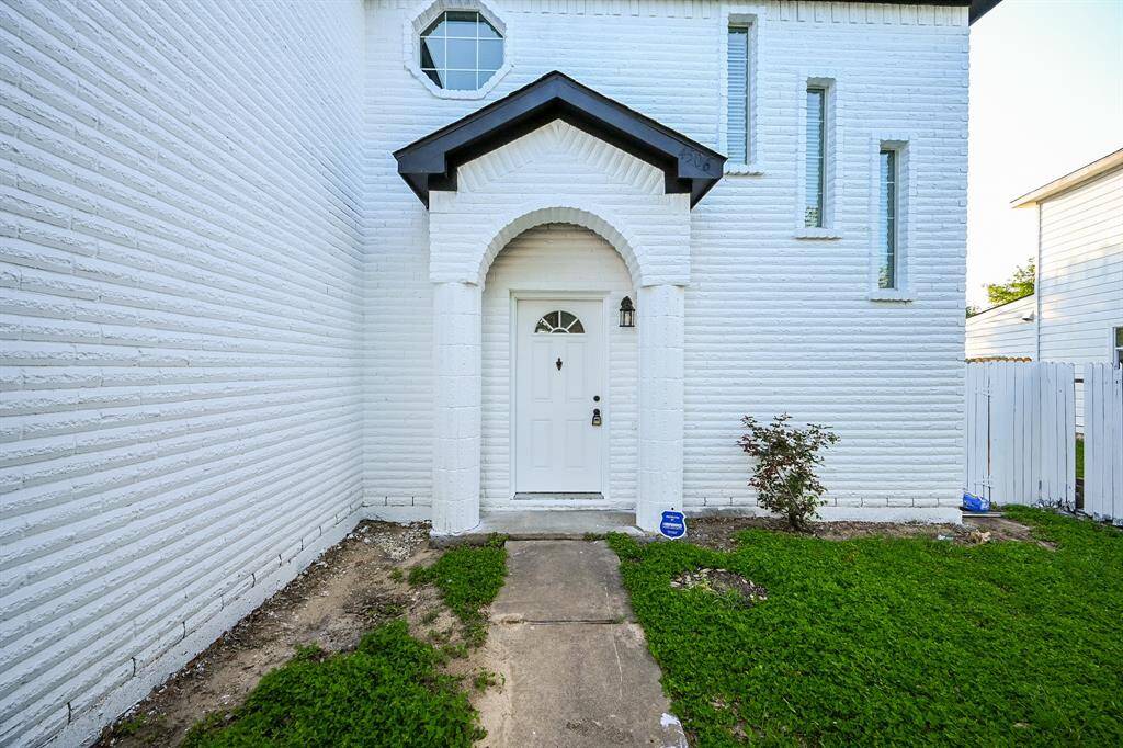 This home features a welcoming entrance with a white brick exterior, arched doorway, and a small front garden area. The front door is adorned with a decorative window and flanked by narrow vertical windows.