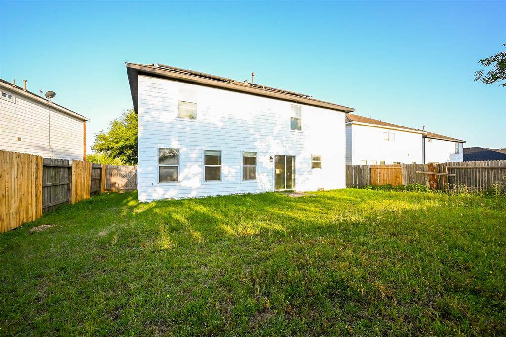 Backyard of this two-story house with white siding, featuring a spacious grassy area enclosed by a wooden fence. The area is well-lit with natural sunlight, creating a bright and inviting outdoor space.