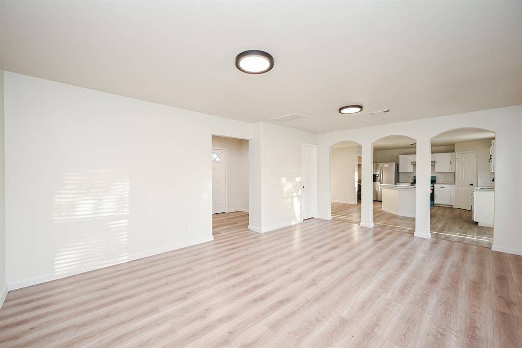 This spacious living area features light wood flooring, neutral walls, and modern ceiling lights. It seamlessly connects to an open kitchen with arched entryways, offering a bright and inviting space for entertaining.