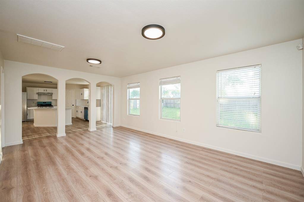 This spacious living area features laminate wood flooring, ample natural light from large windows, and seamless access to the kitchen through stylish archways.