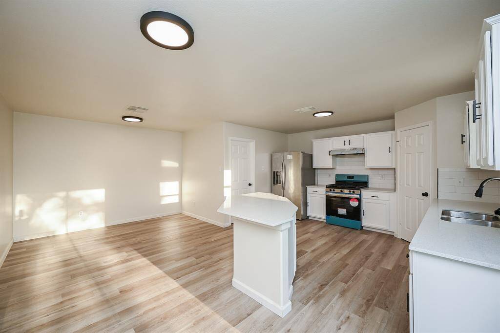 Bright and spacious kitchen with modern appliances, white cabinetry, and light wood flooring. The open layout offers ample space for dining and entertaining.