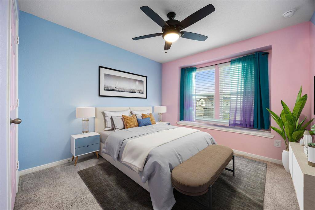 Secondary bedroom features plush carpet, custom paint, dark stained ceiling fan with lighting and a large window with privacy blinds. *virtual staging*