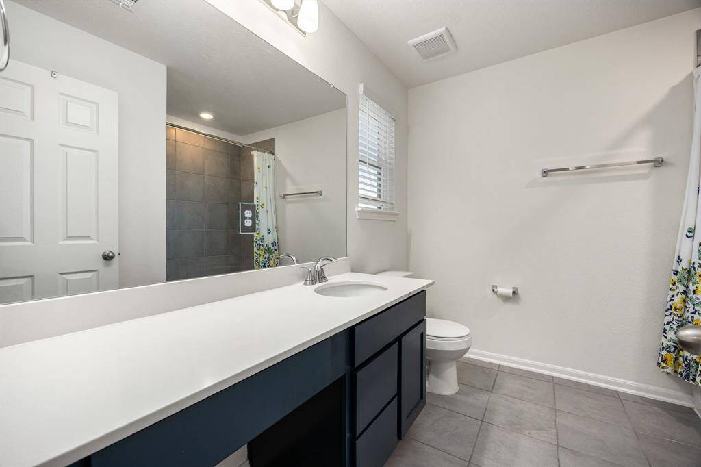 Secondary bathroom features light countertops and dark cabinets, neutral paint, shower/tub combo with tile surround, large mirror, tile floors, sleek fixtures and plenty of space to accommodate any visiting family or guests.