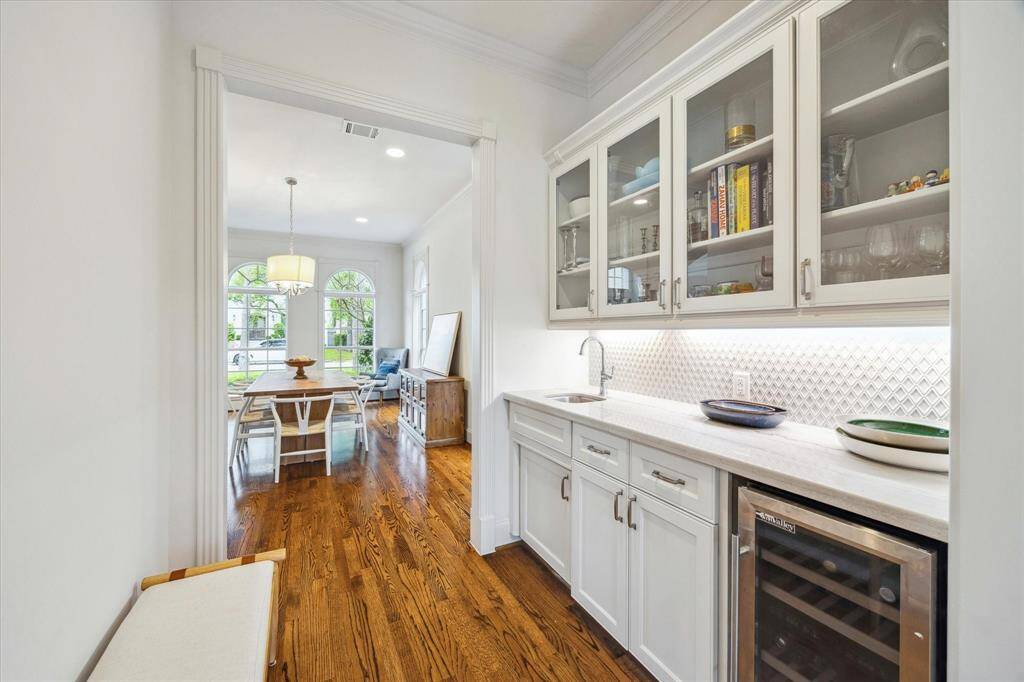 The butler's pantry is adorned with sleek quartz countertops, a striking harlequin-style backsplash, wine refrigerator and elegant glass-front cabinets. A cased opening seamlessly connects the space to the dining room.