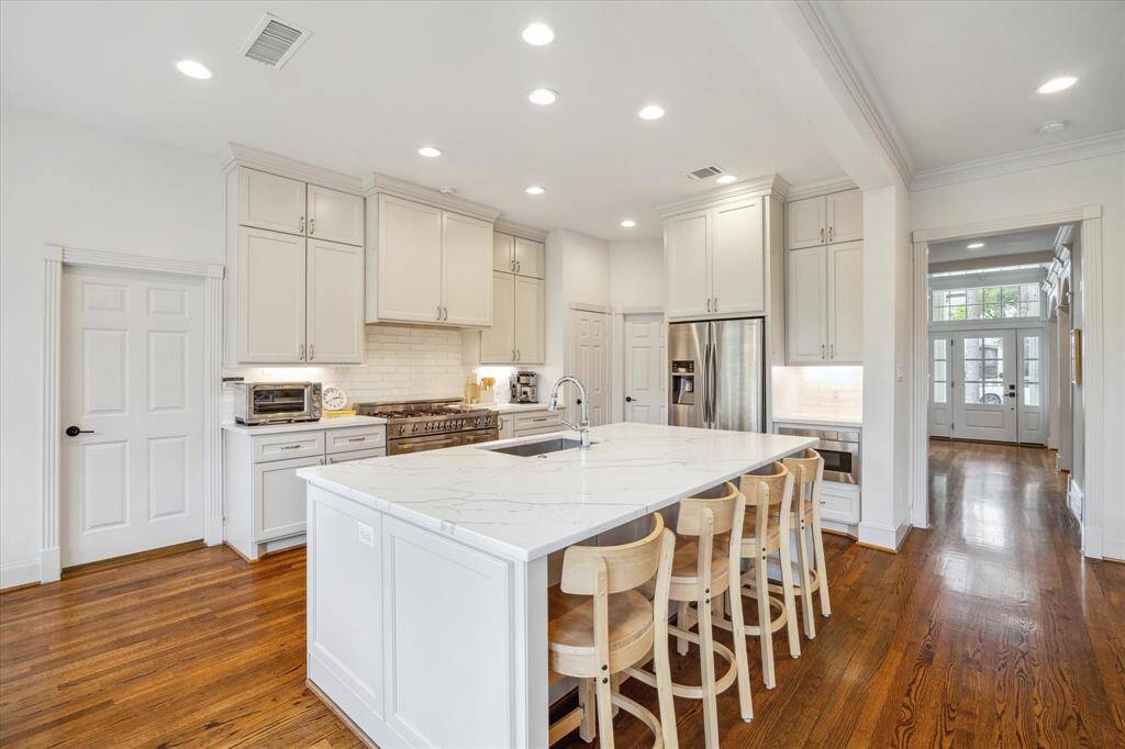 The kitchen is highlighted by recessed lighting, a large island with breakfast bar seating, cabinets that extend to the ceiling, and premium stainless appliances, including a microwave drawer. It also boasts a walk-in pantry and a nearby mudroom.