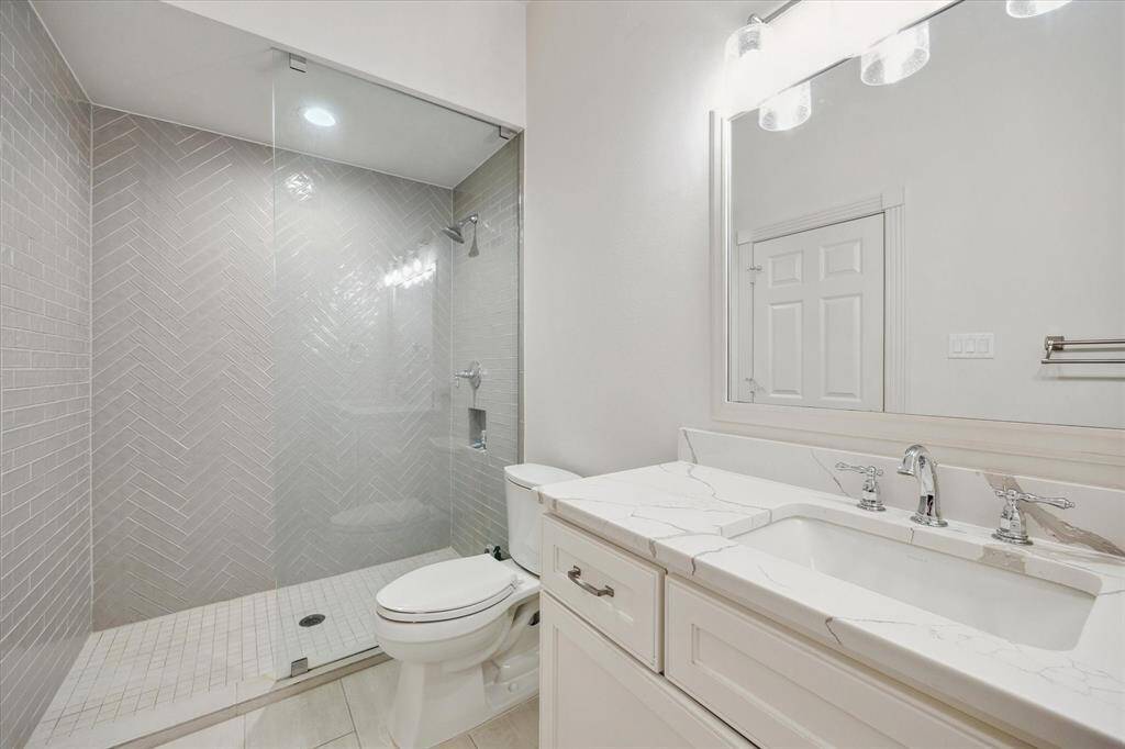The bathroom adjacent to the downstairs bedroom features a spacious walk-in shower, custom cabinetry with sleek quartz countertops, and a built-in shelving niche.