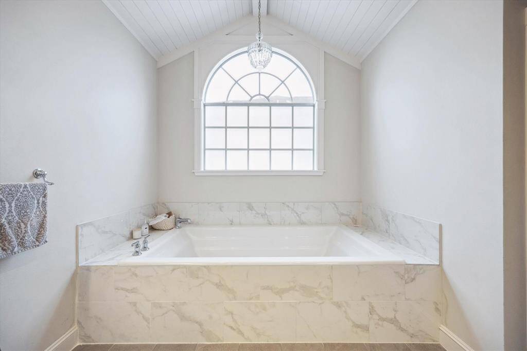 Unwind in the serene soaking tub, framed by a chandelier above and a large window that floods the space with natural light, creating a tranquil escape.