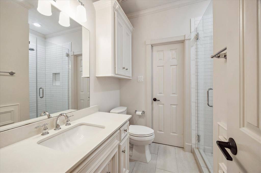 The en-suite bath features sleek quartz countertops and a subway tile shower with a frameless glass enclosure. The closed door leads to a spacious walk-in closet.