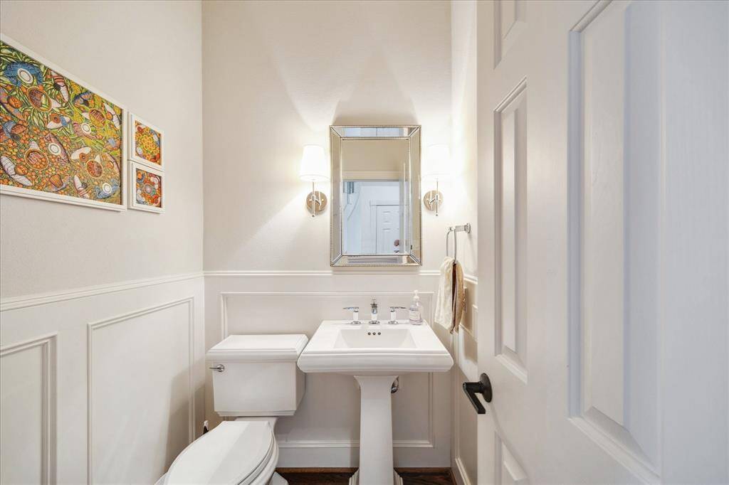 The powder bath has been thoughtfully upgraded with a new pedestal sink, elegant wainscoting, and dual wall sconces. Behind the door, discreet storage is provided for bathroom essentials.