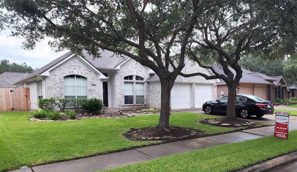 A welcoming facade framed by a spacious, well-manicured lawn, accented with neatly trimmed plant beds and trees. The attached two-car garage sits conveniently beside the greenery, blending function with curb appeal.
