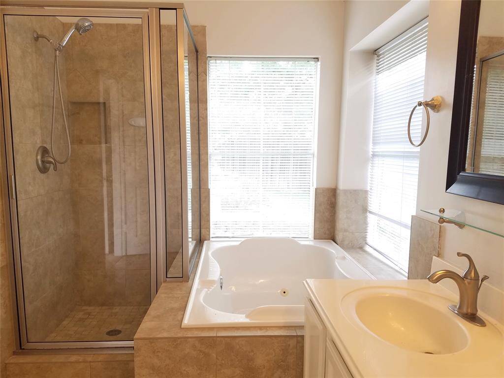 The primary bathroom is a thoughtfully designed oasis featuring a jetted tub beneath oversized windows, bringing in natural light. The glass-enclosed shower offers a sleek touch, while the vanity provides under-storage for effortless organization.