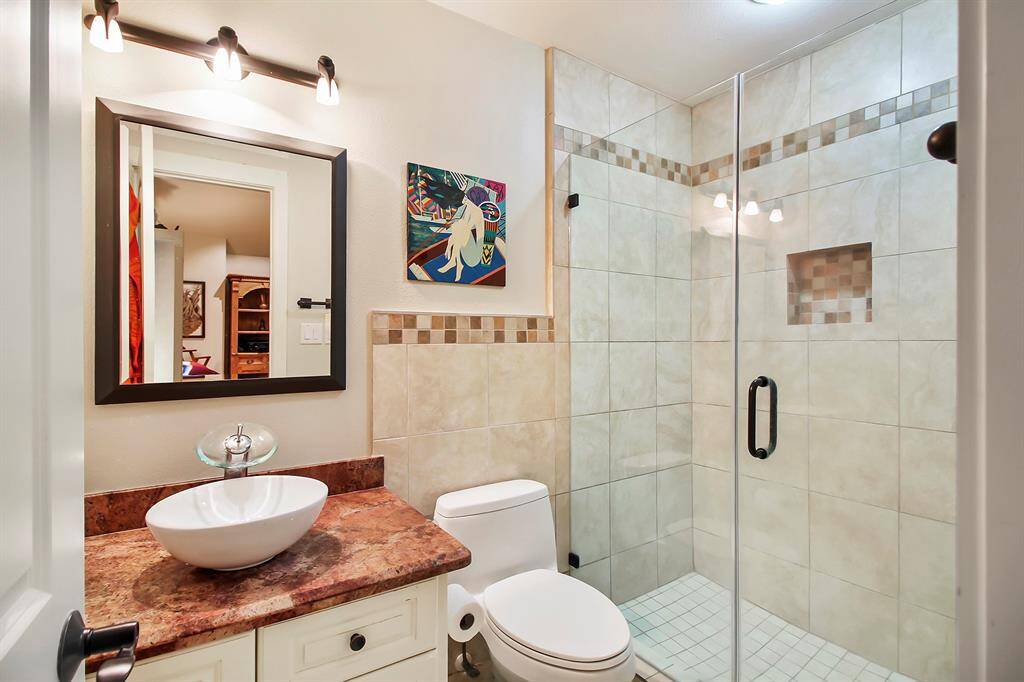 En suite bathroom serving the bedroom/study area with a tile walk-in frameless glass shower. This bathroom is a 2012 addition complete with granite countertop, round bowl hand washing basin.