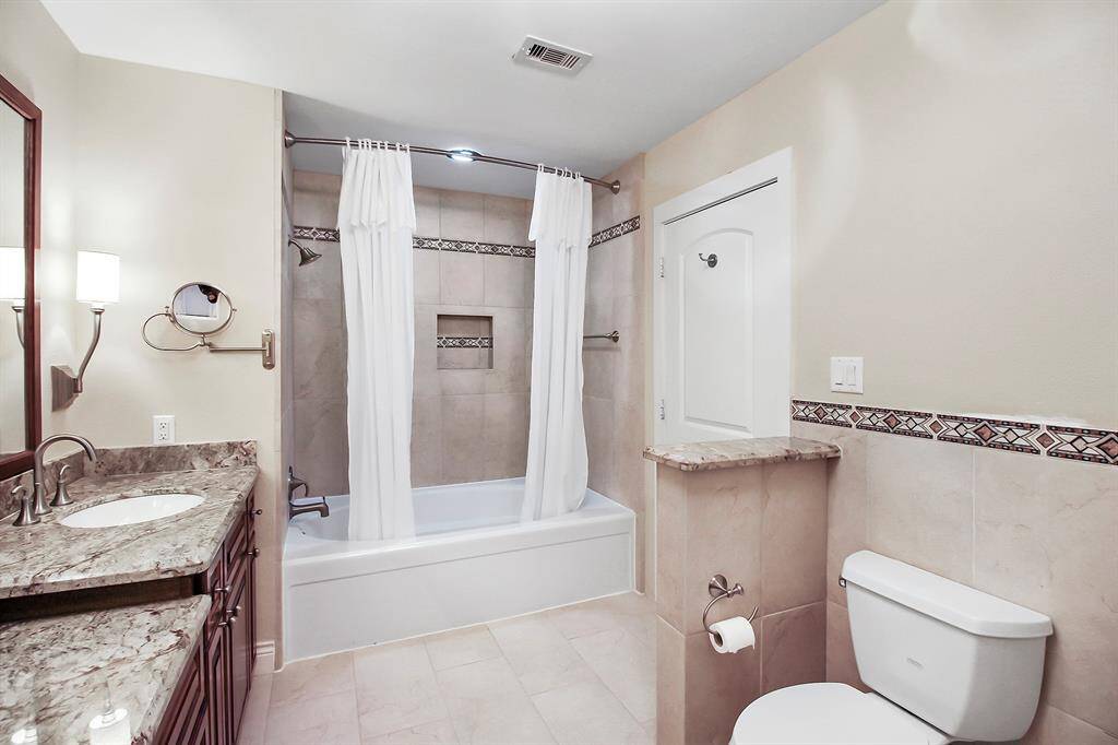 Here is another view of the en suite master bathroom, showing a large size tub/shower combo and matching tile and accent tiles throughout.
