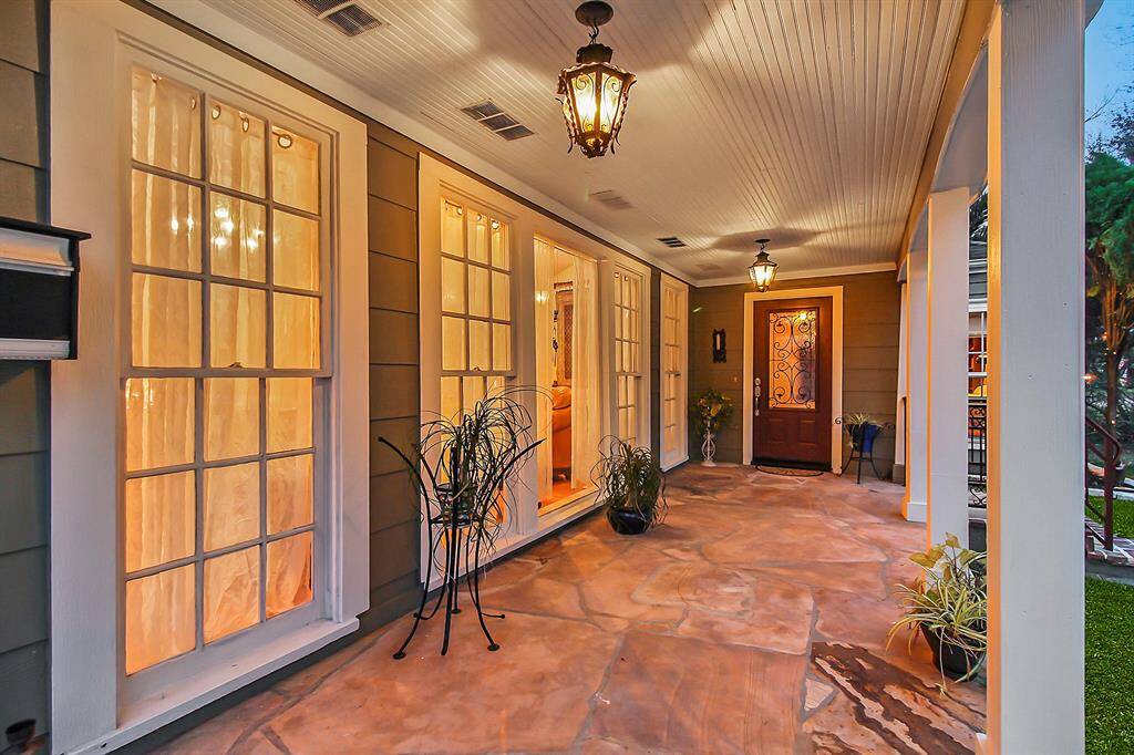 We enter the main house through the main entrance. Inviting, large covered front yard porch. Notice the flagstone floor and rustic lights. Floor to ceiling windows provide plenty of light to the living area inside!