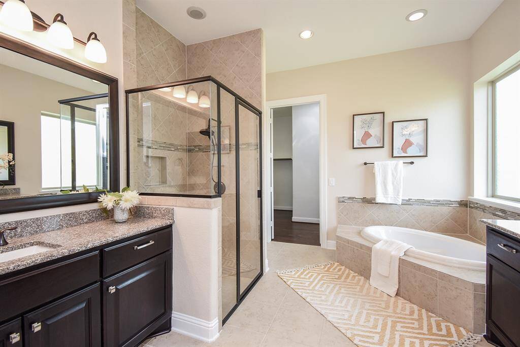 The en-suite bath feels like your own private spa, featuring a soaking tub by the window, a separate glass-enclosed shower, dual vanities, and rich dark cabinetry—all filled with natural light for a serene start or end to your day.