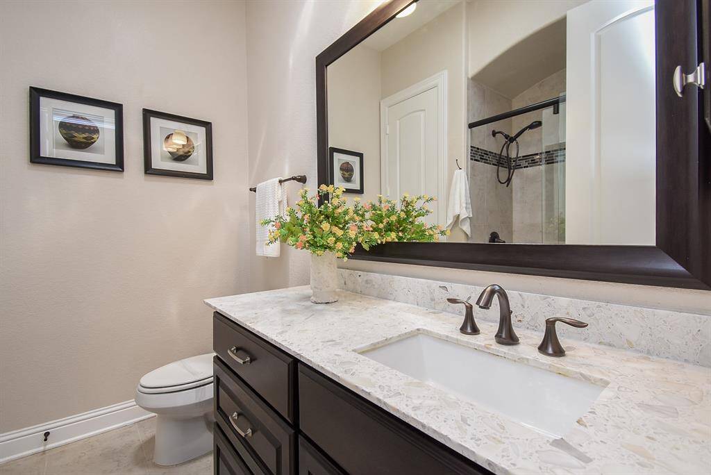 This elegant full bathroom, shared by both secondary bedrooms, features a sleek quartz countertop, rich dark cabinetry, and a tiled shower with a sliding glass door—designed for comfort and convenience. A skylight above bathes the space in natural light, enhancing its warmth and creating a serene, spa-like ambiance.