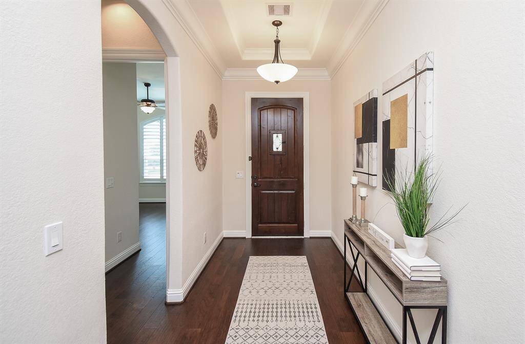 A rich wood front door with a wrought iron inset opens to a bright entryway featuring crown molding, soft lighting, and dark wood floors. The arched doorway and crisp white trim add warmth and elegance to this welcoming space. Skylights were also added to enhance the natural light throughout the home.