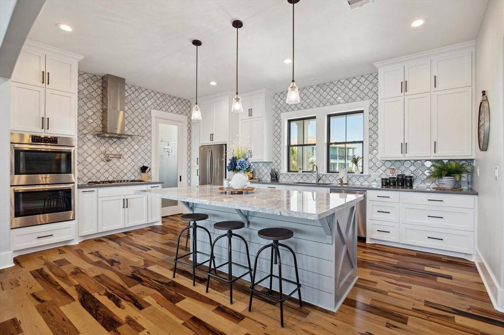 This chef’s kitchen impresses with Quartz countertops, a custom island, high-end Bosch appliances—gas range, exhaust hood, double ovens, and dishwasher...Notice the tiled accent walls