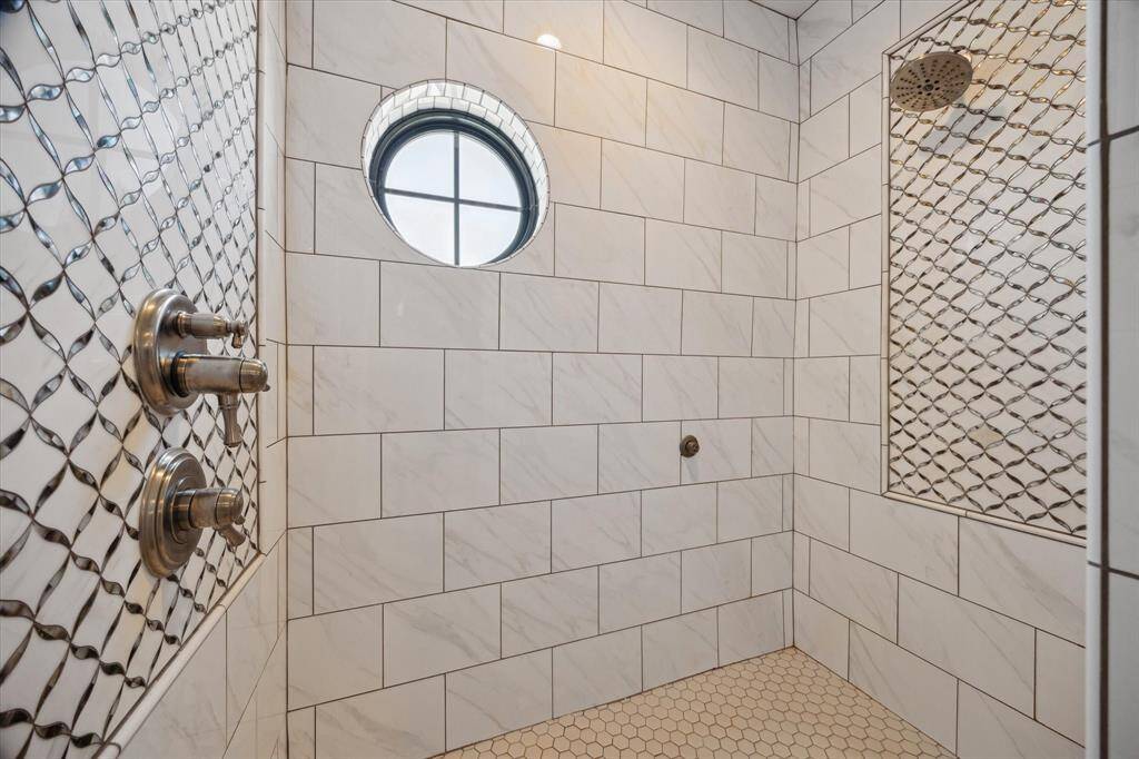 Step into the spa-like primary bath’s custom-tiled shower, featuring elegant coastal design and generous space. Multiple shower heads provide a truly indulgent experience, while a charming porthole window adds natural light and a unique nautical touch