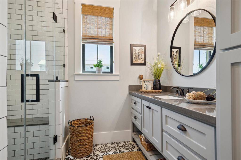 The second bathroom offers a vanity with shaker-style cabinetry topped with sleek countertops, accented by matte black fixtures and a mirror under elegant glass pendant lighting. Patterned tile flooring & subway-tile shower along with a frameless glass door provides a clean, timeless look